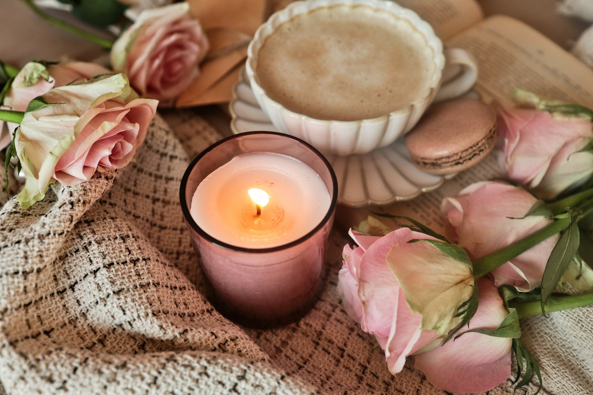 A lit candle beside a latte, pink roses and macarons